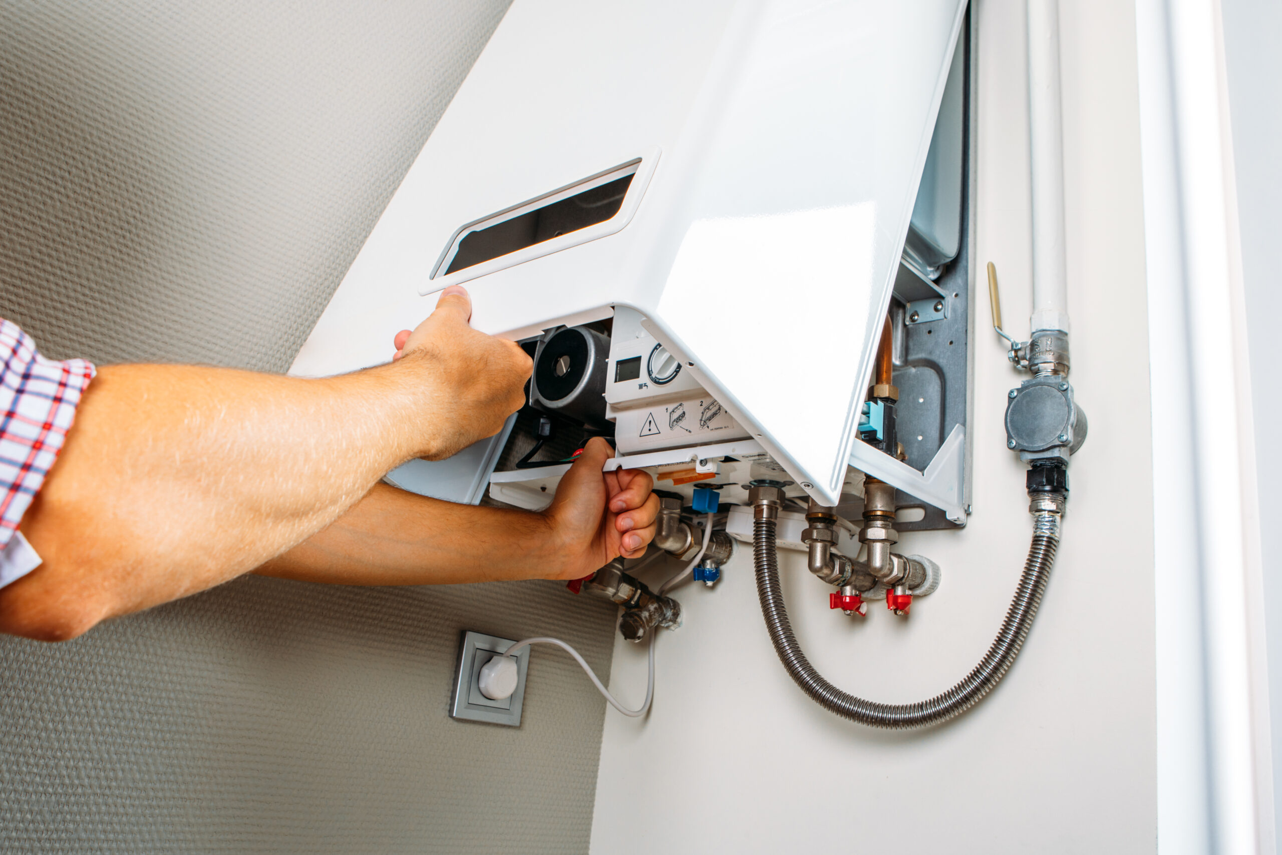 Technician repairing a water heater, adjusting internal components with tools and exposed wiring in a utility room.